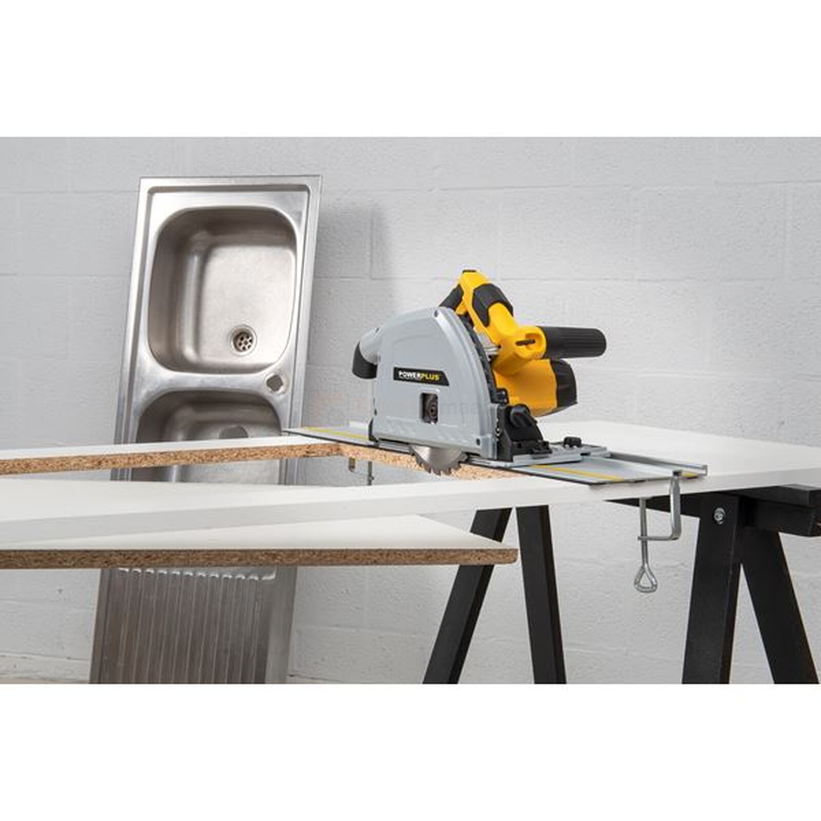 Pildil on Powerplus X sukeldussaag POWX0562, mis lõikab valget plaati, samal ajal kui taustal on valamu ja töölaud.